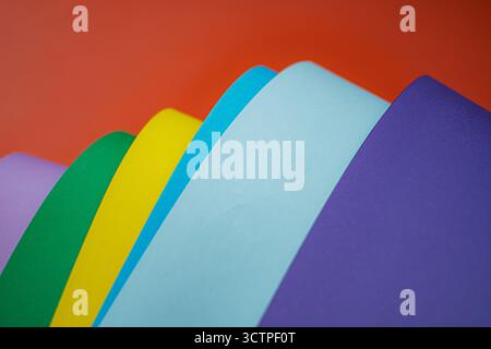Curved sheets of multicolored paper arranged in layers against a bright red background. The composition highlights vibrant tones. Stock Photo