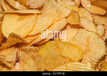 Crispy golden potato chips in a close-up shot. Crunchy salted snack with ridged texture. Perfect for casual eating, parties and fast food cravings. Stock Photo