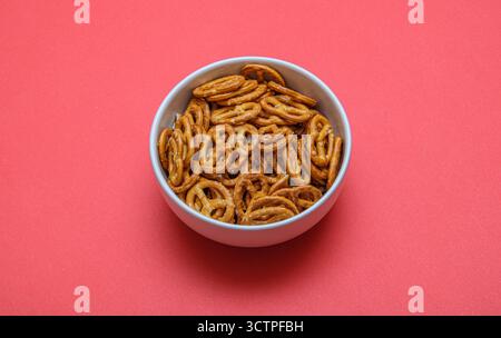 Isolated a simple bowl full of golden pretzels placed on a vibrant pink background. The crunchy and salted snack stands out with its texture. Stock Photo