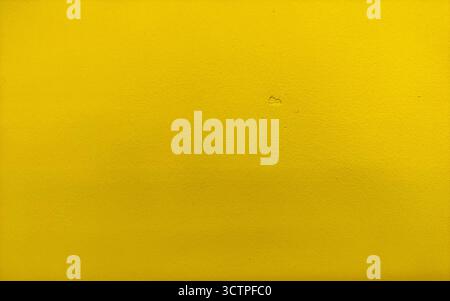 Plain yellow textured wall surface with a small mark at the center. Minimal background with a bright and vibrant tone. Suitable for creative design. Stock Photo