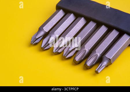 Set of metallic screwdriver bits, including Phillips and Torx are neatly arranged in a black holder against a bright yellow background. Stock Photo