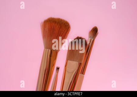 Set of makeup brushes with rose gold handles against a soft pink background. The fluffy bristles and sleek design symbolize beauty and cosmetics Stock Photo