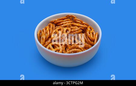 White bowl filled with crunchy salted pretzels on a solid blue background. The golden-brown pretzel snacks stand out. Highlighting texture. Stock Photo