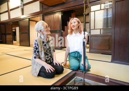 Two women sitting on the floor, one of them is wearing glasses. The woman on the left is older and the woman on the right is younger. They are looking Stock Photo