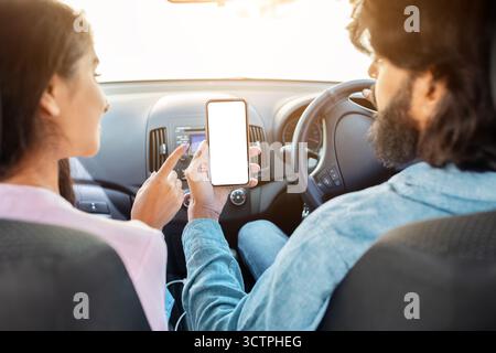 Indian couple using smartphone with blank white screen in car, discussing app Stock Photo