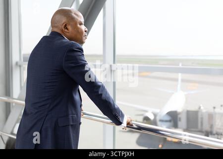 Mature African American businessman standing by airport window, watching airplanes on runway Stock Photo