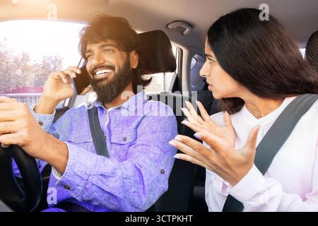 Frustrated Indian woman gesturing while man talks on phone while driving Stock Photo