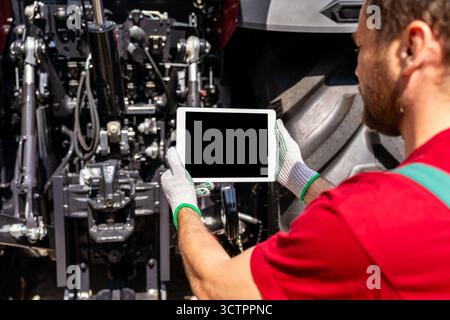 Agricultural machinery mechanic using digital tablet to inspect tractor. Stock Photo