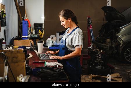 Female auto mechanic working on laptop in local car repair garage. Stock Photo