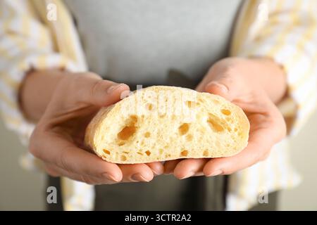Woman holding half of fresh ciabatta on light background, closeup Stock Photo