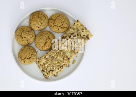 A white plate with oatmeal cookies and seed crackers served next to a cup of black coffee on a white background. Minimalist breakfast or snack concept Stock Photo