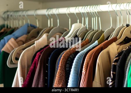 Close up of female warm knitted cloths on hangers in the closet  Stock Photo