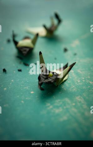 Burnt origami birds on textured green surface symbolizing fragility, destruction, and artistic expression Stock Photo