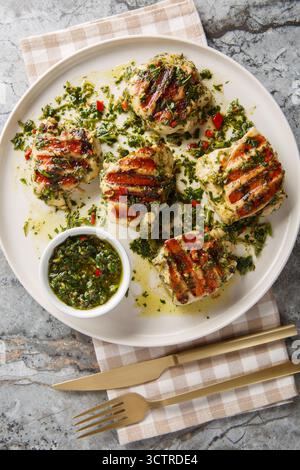 Grilled chicken thighs with Argentinian chimichurri sauce closeup on the plate on the table. Vertical top view from above Stock Photo