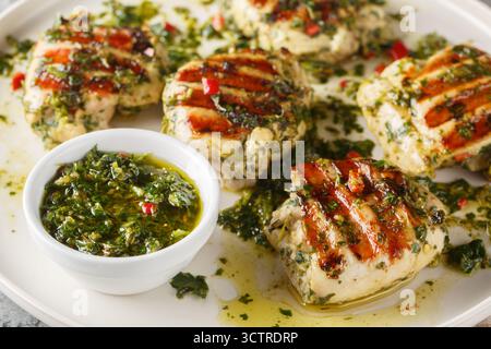 Grilled chicken thighs marinated and drizzled with chimichurri sauce, close-up on a plate on a table. Horizontal Stock Photo
