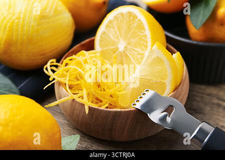 Lemon zest in bowl, fresh fruits and zester tool on table, closeup Stock Photo