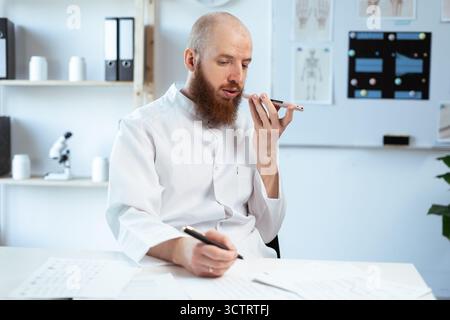 Young bearded male doctor using smartphone in hospital and sending an audio message to a patient Stock Photo