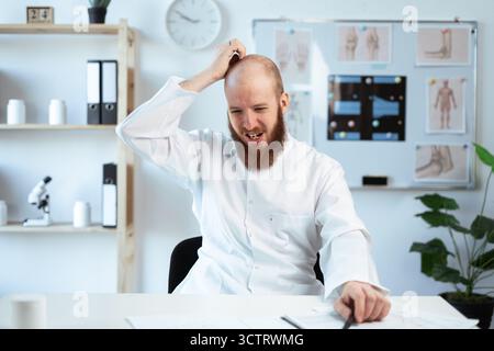 sad puzzled confused bearded doctor scratch head looking aside while working in hospital or medical clinic Stock Photo