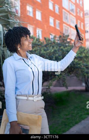 Smiling Afro american woman happily taking selfie in urban setting. Vertical frame Stock Photo