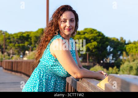 Smiling woman leaning on wooden bridge railing outdoors enjoying summer day Stock Photo