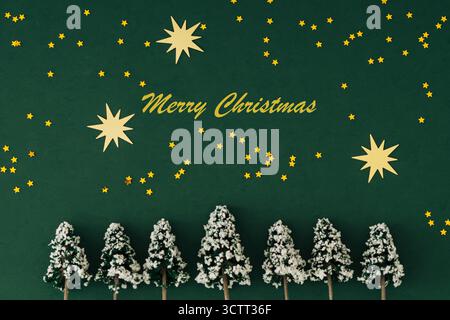 Winter composition with golden star glitter confetti and Xmas trees on green background. Minimal Christmas and New Year concept. Stock Photo