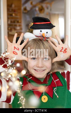 A smiling, happy-faced child in festive attire. The numbers for the new year 2026 are written on his palms. Christmas, happy winter holidays, the comf Stock Photo