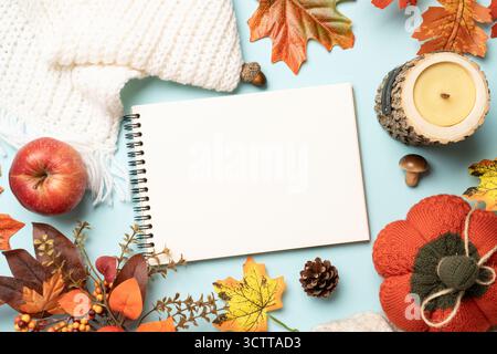 Autumn flat lay background, thanksgiving day concept. Falling leaves, notepad, knitted scarf and wooden candle on blue background. Stock Photo