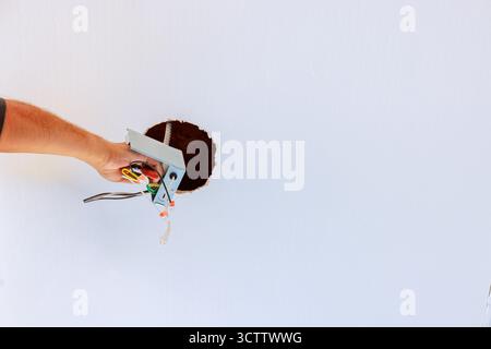 Electricians is reaching through hole in ceiling, working on electrical wires during home repairs. Stock Photo