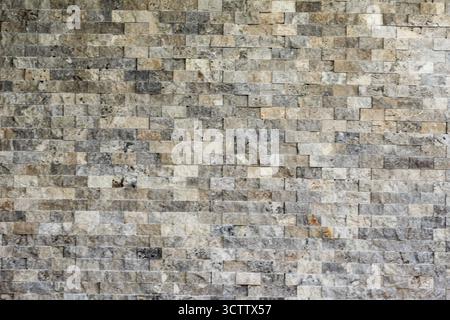 Close-up of a natural stone wall with rough gray and beige tiles, creating a rustic and textured background perfect for design or architecture project Stock Photo