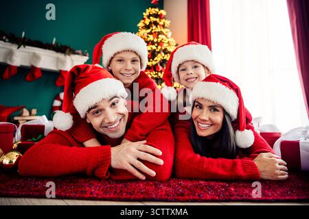 Happy family of four in festive sweaters celebrating Christmas together at home near a decorated Christmas tree Stock Photo