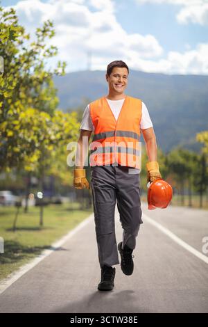 Construction worker in a reflective vest holding a hardhat and walking in a park Stock Photo