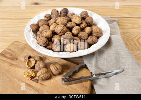 Still life of Walnuts in a white bowl with a nutcracker on a wooden board Stock Photo