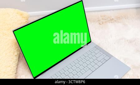 Laptop mock up featuring a vibrant green screen placed on a soft fur rug, ideal for showcasing digital content and creative design projects Stock Photo