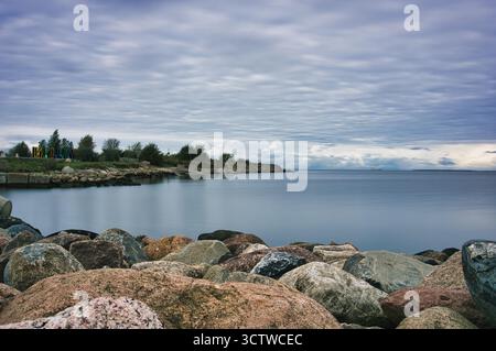 Dramatic Cloudy Sky Over Calm Sea with Rocky Shoreline in Foreground Stock Photo