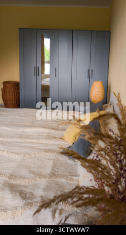Modern bedroom interior featuring a bed, gray wardrobe, and warm decorative accents. The composition conveys comfort and minimalism in a soft light. Stock Photo