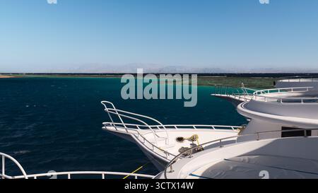 A beautiful seascape. The bows of white yachts face the clear turquoise waters, gradually fading to deep blue. In the distance, the faint silhouettes Stock Photo