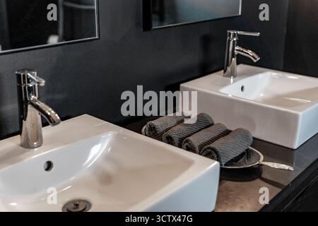Close-up of white dual vanity sinks and gray towels in modern black bathroom Stock Photo