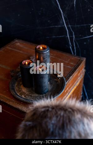Black candles burning flame on silver pewter platter on old leather trunk with fur in foreground Stock Photo
