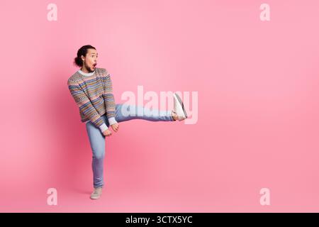 A Surprised Stylish Young Man in a Colorful Sweater Against a Pink Background Striking a Unique Pose with a Gesture of Awe and Excitement. Stock Photo