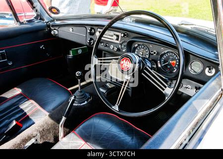 Interior view of a classic MG  MGB GT car highlighting the vintage steering wheel, dashboard, and leather seating with red stitching accents Stock Photo