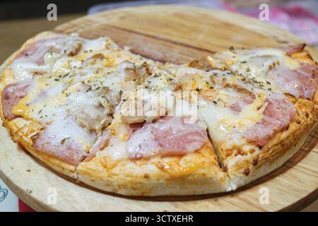 Close-up of a cheese, ham, and sausage Pizza on a wooden tray. Six slices remaining. A popular Thai street food snack. Stock Photo