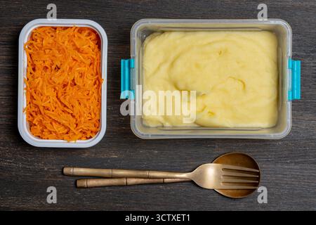 Several dishes in plastic boxes for breakfast on a wooden table, close up, top view. Mashed potatoes and grated carrots in plastic food containers Stock Photo