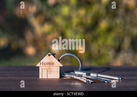 House keys on a wooden house shaped keychain on wooden table, outdoors, close up, copy space. Real estate concept of buying or renting a home Stock Photo