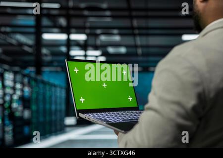 Close up of system administrator in data center using green screen laptop to check for server performance issues. IT expert in server farm fixing errors slowing down hardware using mockup notebook Stock Photo