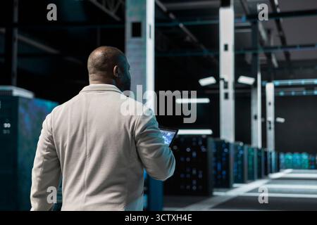 Server hub software developer uses machine learning on device to predict future gear needs. Data center computer scientist using AI neural networks tech on tablet to enhance operational effectiveness. Stock Photo