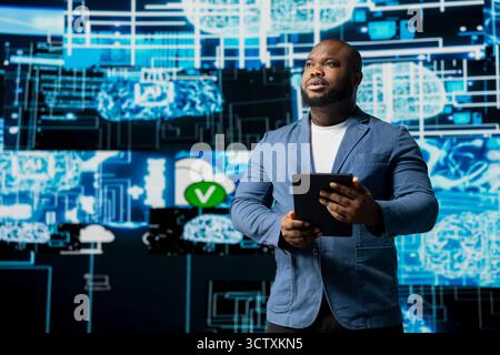 Black male IT engineer examining digital AI brain interface on dashboard, symbolizing neural networks, science and algorithmic thinking. Cybernetics for a high tech machine learning innovation. Stock Photo