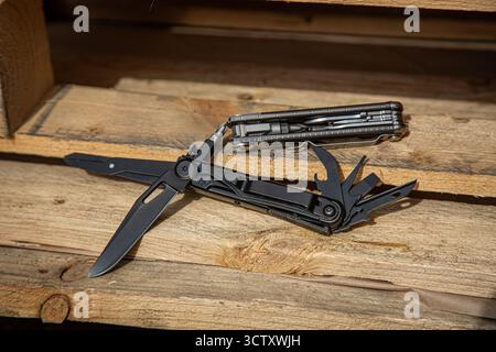 Two tactical multi-tools, one open and black, the other closed and silver, on wooden planks. Stock Photo