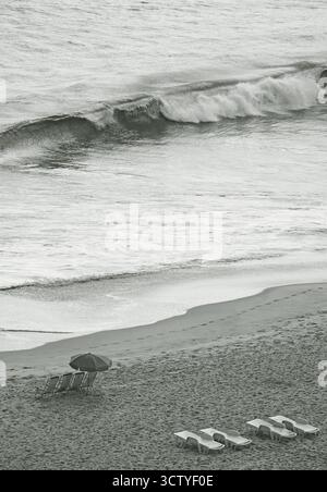 Big waves crashing empty beach with chairs and sunshade in monochrome image Stock Photo