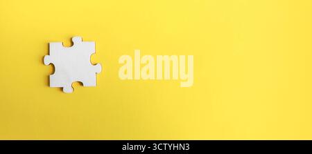 Single white jigsaw puzzle piece on a vibrant yellow background with vast copy space, symbolizing a missing solution, unique idea, and challenge. Stock Photo