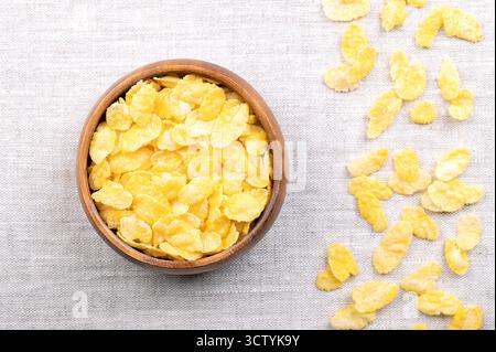 Corn flakes, or cornflakes in a wooden bowl on linen, from above. Breakfast cereal made from toasting flakes of corn or maize. Stock Photo